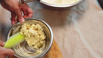 Top view of a pastry chef heating melting callets of white confectionery chocolate in a bain-marie, preparing icing or glaze to decorate cakes, or adding to whipped cream when making mousse desserts video