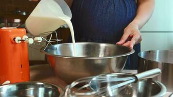 närbild hemmafru häller färsk grädde in i en metall skål för spöstraff med mixer eller vispa. de bearbeta av framställning utsökt mousse efterrätt. kulinariska. matlagning. konfektyr. bageri video