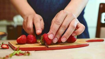 Close-up hands cut fresh ripe organic strawberries in halves on a wooden board in home kitchen, for decorating a mousse dessert Fraisier. Healthy eating. Dieting. Berries and fruits. Vegetarian food video