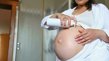 fechar-se barriga do grávida mulher desenha uma coração forma enquanto apertando hidratante loção, massageando dela barriga para reduzir esticam marcas dentro gravidez tempo, durante manhã spa procedimentos dentro casa banheiro video