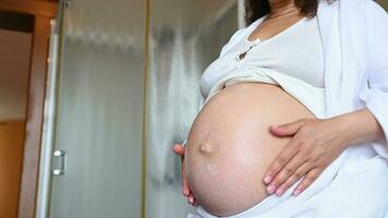 midsection av en gravid förväntans kvinna masse henne gravid mage, gnuggning sträcka märken kosmetika i de Hem badrum. Hem spa procedurer, hud och kropp vård i graviditet tid. hygien begrepp video