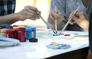 asian middle aged female hand teaches asian teenage boys mixing the watercolors in the palette on table, teacher helping teenager students to do artwork at school photo