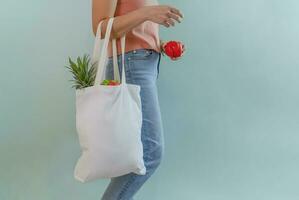 young female carrying reusable cloth bag of fruits and vegetables isolated on blue background, concept for campaign of using reusable bag, reduce waste, stop global warming, save the world photo