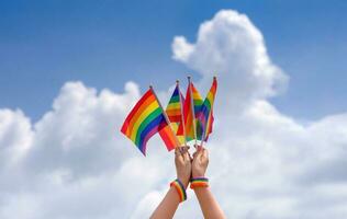 people hand holding lgbt colorful rainbow gay flag background blue sky photo