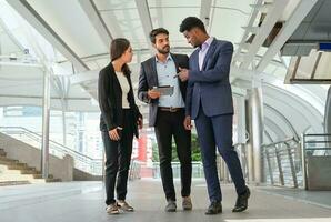group of young multiracial business people chatting and looking at tablet online work while walking outside photo