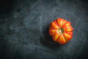 Red ribbed tomato cuore di bue on a dark background top view photo