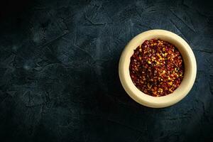 Dried red pepper flakes in a wooden bowl. Chili pepper flakes on a dark background. Top view photo