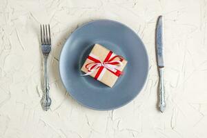 Christmas table setting with grey plate, gift box and silverware on light background photo