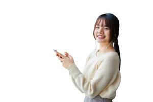 Cute young Asian student wearing long-sleeved shirt is standing and smiling while using her smartphone and headphones to listen lecture confidently while isolated on white background. photo