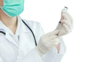 Professional asian woman doctor is using syringe to suck vaccine Coronavirus vaccine from bottle while her hands wear rubber gloves and face mask while isolated on white background.. photo