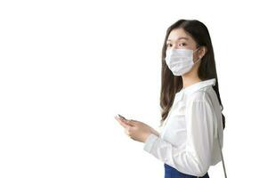 Young Asian business woman is going to the office or workplace which she look at camera while wearing mask holds smartphone in her hands in big city while isolated on white background. photo