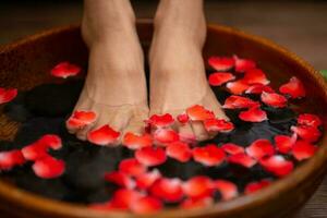 mujer empapa su pies en un cuenco con flor pétalos foto