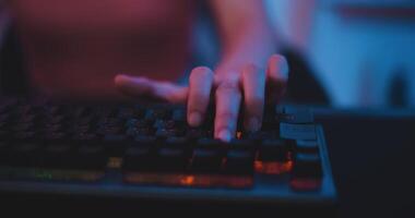 Footage close-up keyboard of Young Asian esport women gamers playing online video games on the computer with neon light at home. Girl gaming player feels enjoy technology broadcast live streaming.