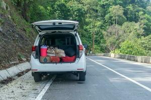 maletero de el coche lleno con suministros para fin de semana la carretera viaje. picnic concepto. suv estacionado lado el la carretera foto