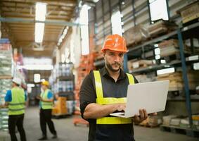 Professional manager man employee using laptop check stock working at warehouse. Worker wearing high visibility clothing and a hard hat, helmet and checking and count up goods or boxes for delivery. photo