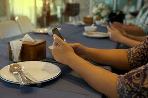 Customers are surfing the internet on their mobile phones while waiting for dinner to be ordered at the table. soft and selective focus. photo