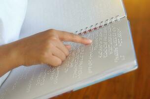 visualmente dañado persona lee con su dedos un libro escrito en braille eso es escrito para esos quien son visualmente dañado o ciego. eso es un especial código generado desde 6 6 puntos en el caja. foto