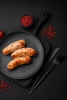 Delicious juicy grilled sausages with salt, spices and herbs on a ceramic plate photo