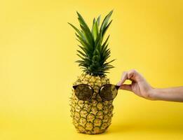 Young woman hand holding sunglasses, nutritious pineapple, vacation travel concept - yellow background photo