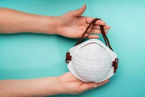 Hands of a young woman holding a medical mask to prevent respiratory diseases and various viruses - turquoise background photo