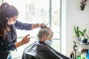 mayor mujer consiguiendo un Corte de pelo a hogar durante covid19 pandemia vistiendo cara máscara foto