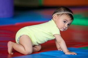 hermosa diez meses bebé niña gateando en un vistoso antecedentes. temprano estímulo para niños pequeños concepto. foto