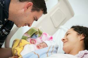 joven madre y padre con su recién nacido bebé niña a el hospital en el día de su nacimiento. familia concepto. paternidad concepto foto
