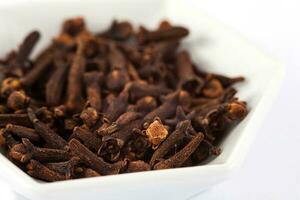 Spice cloves in a small white ceramic dish isolated on white background photo