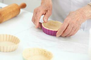 Senior woman preparing dough for a delicious cheese and ham tartlet photo