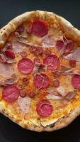 Delicious fresh oven baked pizza with salami, meat, cheese, tomatoes, spices and herbs on a dark concrete background video