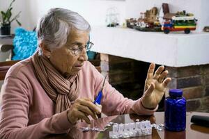 Senior woman at home arranging her prescription drugs into a weekly pill organizer photo