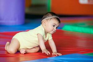 hermosa diez meses bebé niña gateando en un vistoso antecedentes. temprano estímulo para niños pequeños concepto. foto