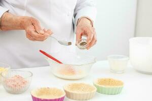 Senior woman preparing the filling for a delicious cheese and ham tartlet photo