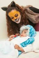 pequeño niña jugando abuela personaje y madre jugando lobo. real familia teniendo divertido mientras utilizando disfraces de el pequeño rojo montando capucha cuento en Víspera de Todos los Santos. foto