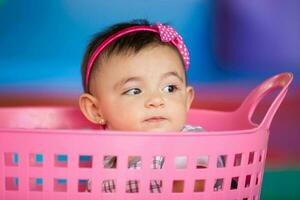hermosa diez meses bebé niña jugando en un rosado cesta. temprano estímulo para niños pequeños concepto. foto