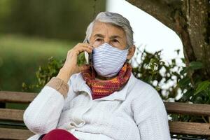 Senior woman outdoors using her cell phone wearing a home made face mask during the coronavirus quarantine de escalation photo