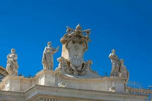 detalle de el chigi abrigos de brazos y el estatuas de santos ese corona el columnatas de S t. pedro cuadrado construido en 1667 en el Vaticano ciudad foto