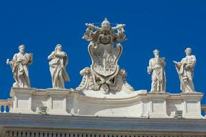 detalle de el chigi abrigos de brazos y el estatuas de santos ese corona el columnatas de S t. pedro cuadrado construido en 1667 en el Vaticano ciudad foto