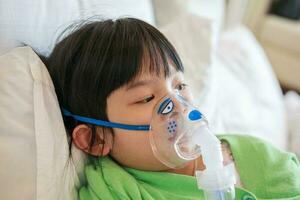 Sick little asian girl inhalation with nebulizer for respiratory treatment photo