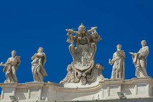 detalle de el chigi abrigos de brazos y el estatuas de santos ese corona el columnatas de S t. pedro cuadrado construido en 1667 en el Vaticano ciudad foto