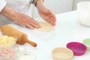 Senior woman preparing dough for a delicious cheese and ham tartlet photo