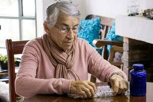 Senior woman at home arranging her prescription drugs into a weekly pill organizer photo