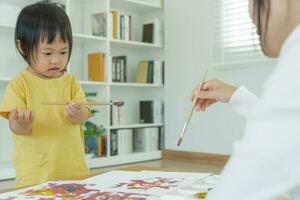 contento Asia madre jugando aprendizaje pintar para pequeño muchacha. gracioso familia es contento y emocionado en el casa. madre y hija teniendo divertido gasto hora juntos. día festivo, actividad foto