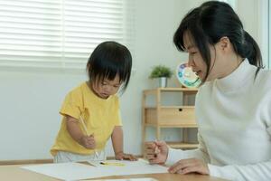 contento Asia madre jugando aprendizaje pintar para pequeño muchacha. gracioso familia es contento y emocionado en el casa. madre y hija teniendo divertido gasto hora juntos. día festivo, actividad foto