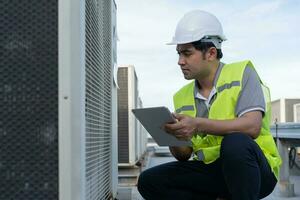 Asian maintenance engineer works on the roof of factory. contractor inspect compressor system and plans installation of air condition systems in construction. technology, online, mobile application. photo
