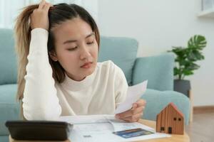 Debt house, Stressed and headache asian woman with large bills or invoices no money to pay, shortage, Financial problems, mortgage, loan, bankruptcy, bankrupt, poor, empty wallet, overdue photo