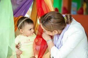 Beautiful ten months baby girl playing with colorful fabrics and her mom. Early stimulation for toddlers concept. photo