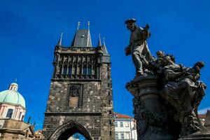 Antique sculpture of Ivo of Kermartin and tower of the medieval gothic Charles Bridge in Prague built on the 15th century photo