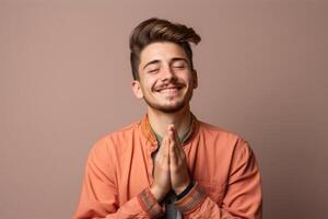 Portrait of a smiling young man praying over brown background photo