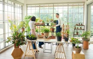 Gardener young Asian man woman two person family stand  smiling lookand helping organize small tree. Inside room  tree leaf green in calm work shop home plant . hobby job happy and care concept photo